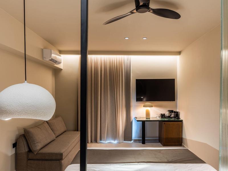 Camera d'hotel moderna con divano, TV, ventilatore a soffitto e luce calda.