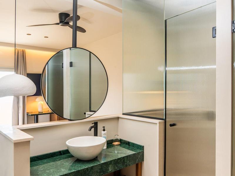 Bagno moderno con specchio rotondo, piano in marmo verde e doccia in vetro.