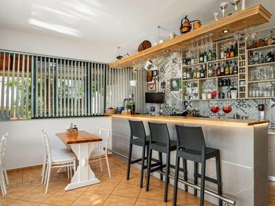 Przytulny bar z drewnianą podłogą, ladą, czarnymi stołkami barowymi i dużym oknem z pionowymi żaluzjami.