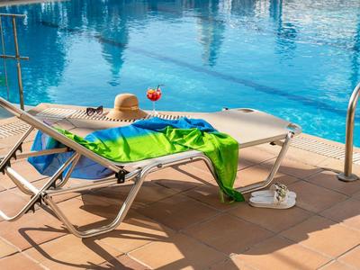 Leżak z zielonym ręcznikiem i słomkowym kapeluszem przy basenie w słoneczny dzień