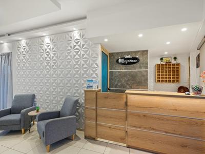 Jasny hol hotelowy z drewnianą recepcją i dwoma szarymi fotelami obok teksturowanej białej ściany.