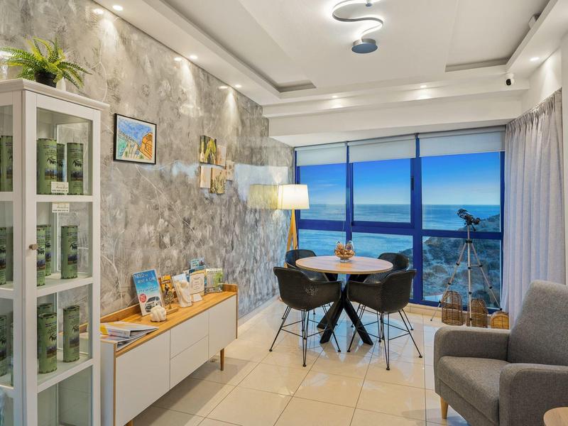 Nowoczesny salon z panoramicznym oknem z widokiem na morze o zachodzie słońca.