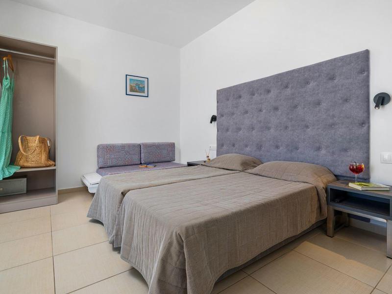 Nowoczesny pokój hotelowy z szarym łóżkiem podwójnym i małym miejscem do siedzenia.