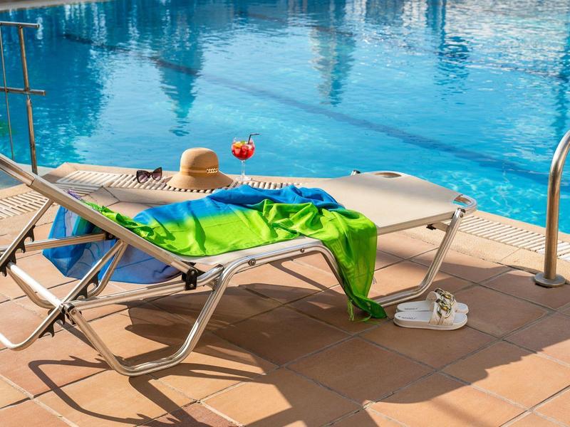 Leżak z zielonym ręcznikiem i słomkowym kapeluszem przy basenie w słoneczny dzień