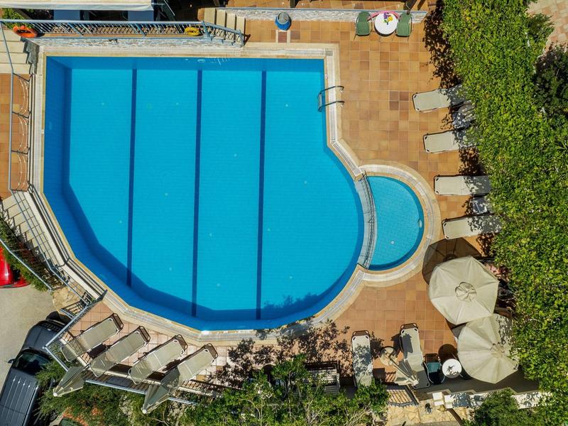 Widok z lotu ptaka na basen z parasolami i leżakami w ogrodzie hotelowym.