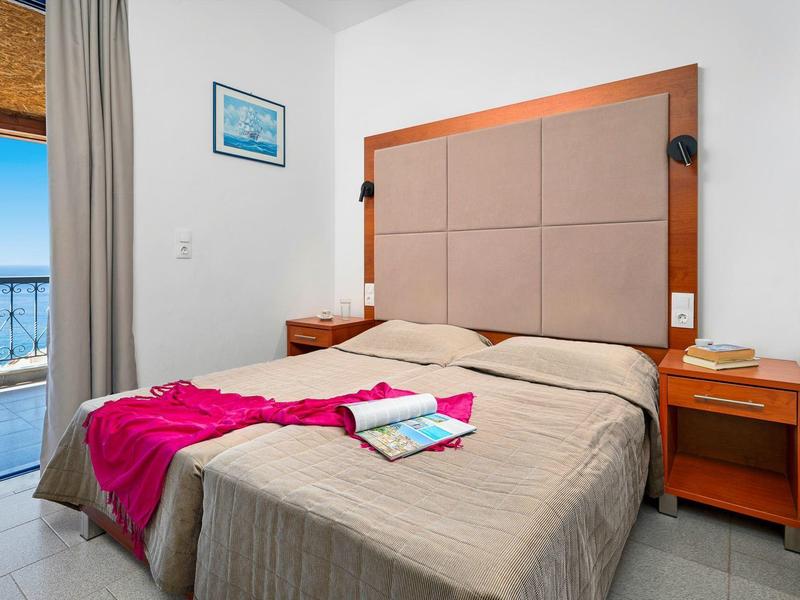 Sypialnia z dużym łóżkiem, stolikami nocnymi i widokiem na balkon i morze.