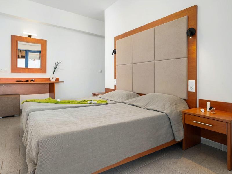 Nowocześnie urządzony pokój hotelowy z łóżkiem podwójnym, stolikiem nocnym i biurkiem z lustrem.