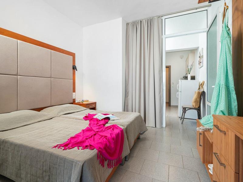 Pokój hotelowy z dwoma pojedynczymi łóżkami, szarą pościelą i różowym szlafrokiem na łóżku.