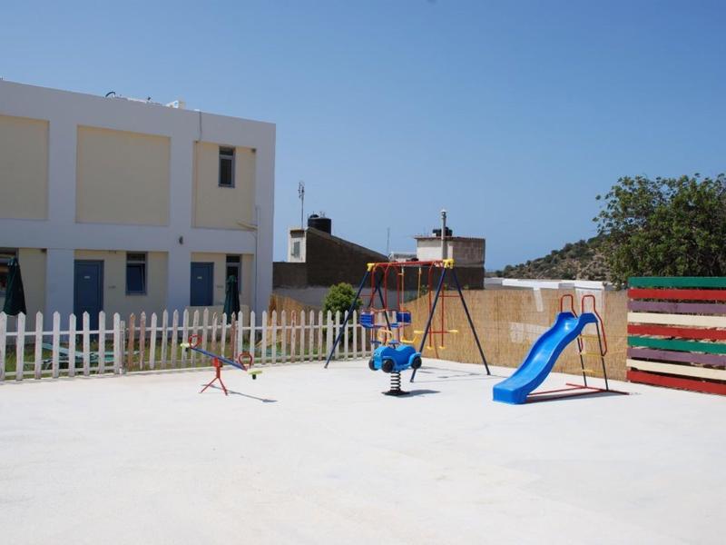 Plac zabaw z huśtawką i zjeżdżalnią przed jasnym budynkiem pod czystym niebem.