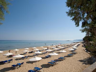 Pláž s řadami slunečníků a lehátek podél pobřeží pod jasnou oblohou.