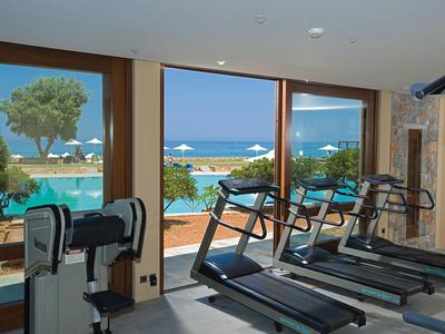 Posilovna s běžeckými pásy s výhledem na bazén a moře skrz velká okna.