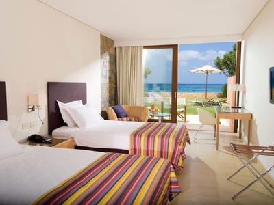 Habitación de hotel luminosa con dos camas y vista al mar a través de grandes ventanas.