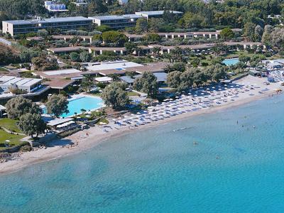 Resort sulla spiaggia con lettini, ombrelloni, piscine e acqua azzurra lungo la riva.