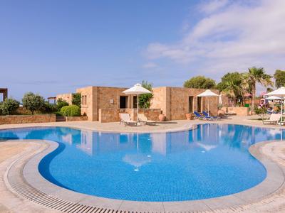 Velký zakřivený bazén s lehátky a slunečníky u hotelu za slunného počasí.