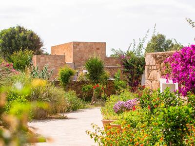 Slunečná zahradní stezka s barevnými květinami a tradičními cihlovými budovami v pozadí.