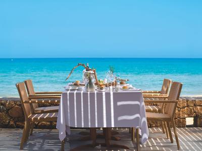 Stůl s bílým ubrusem a židlemi s výhledem na moře v slunečný den.