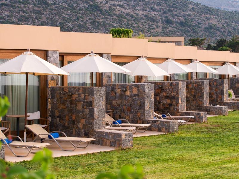 Rząd kamiennych tarasów na zewnątrz z białymi parasolami i leżakami przed pokojami hotelowymi