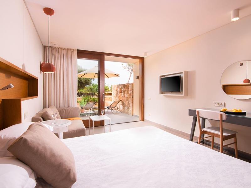 Jasny pokój hotelowy z dużym łóżkiem, częścią wypoczynkową i balkonem z meblami ogrodowymi.