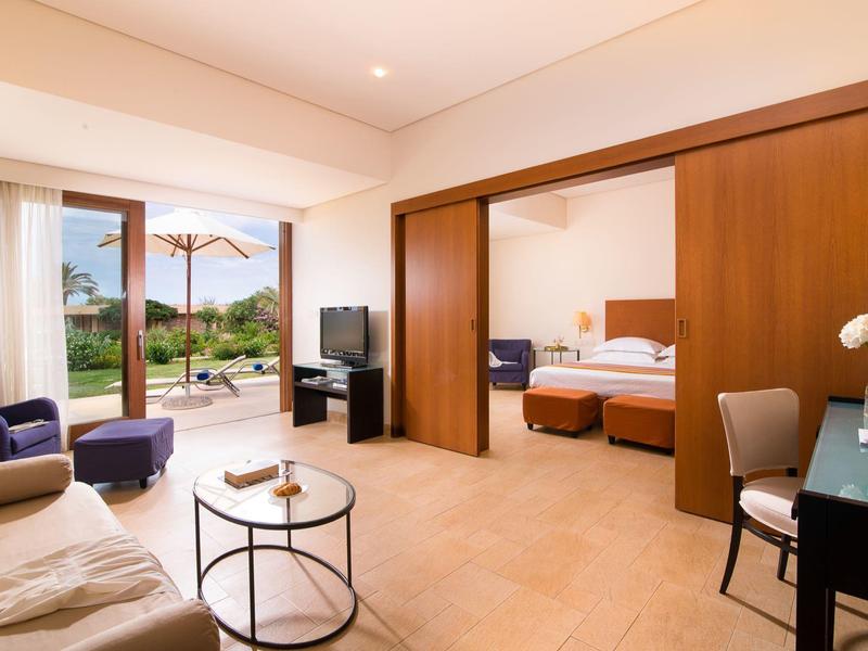 Przestronny apartament hotelowy z częścią dzienną, sypialnią i patio z widokiem na basen i miejsce do siedzenia na zewnątrz.