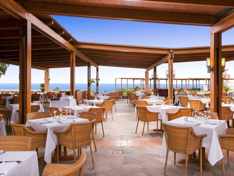 Otwarta restauracja z drewnianą pergolą z widokiem na morze pod bezchmurnym niebem.