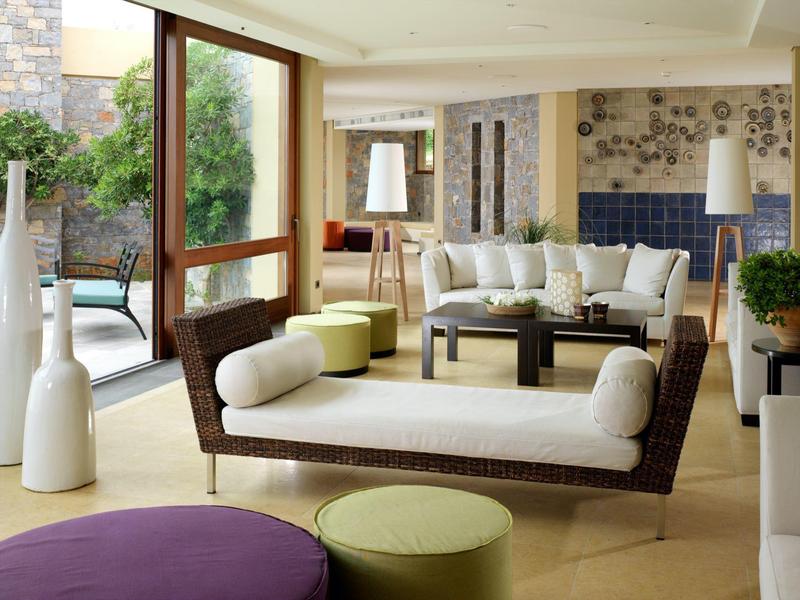 Jasny salon hotelowy z nowoczesnymi białymi i brązowymi meblami przy przesuwnych szklanych drzwiach i patio na zewnątrz.