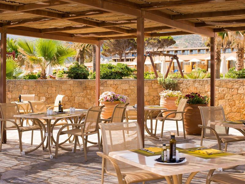 Zewnętrzny taras jadalny z wiklinowymi krzesłami i stołami pod zacienioną pergolą.