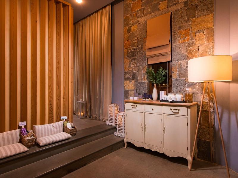 Przytulny pokój spa z dwoma stołami do masażu, ciepłym oświetleniem i dekoracją kamienno-drewnianą.