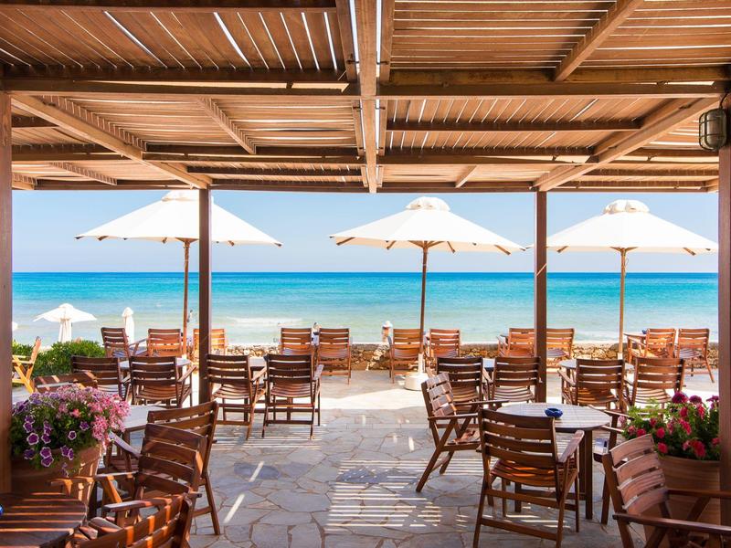 Taras restauracyjny przy plaży z drewnianymi krzesłami, stołami i białymi parasolami nad morzem.