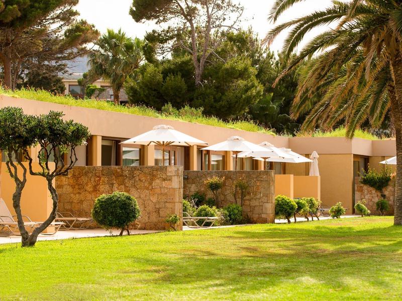 Hotel z parasolami na patio i zielenią pod słonecznym niebem.