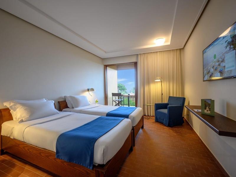 Nowoczesny pokój hotelowy z dwoma łóżkami pojedynczymi, widokiem na morze i miejscem do siedzenia.