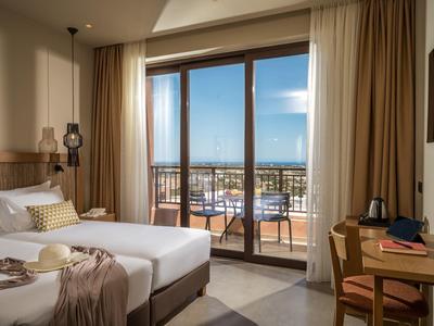 Modernes Hotelzimmer mit Doppelbett, Balkon, Holzmöbeln und Blick auf Stadt und Meer.