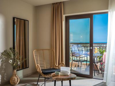 Helles Wohnzimmer mit Sesseln, Tisch, großem Spiegel und Blick auf Balkon bei Dämmerung.