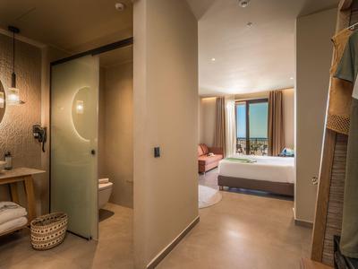 Moderner Hotelflur mit Bad links, Schrank rechts und Blick auf helles Schlafzimmer mit Meerblick.