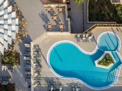 Vogelperspektive auf blauen Pool mit Liegen, Sonnenschirmen und Pflanzen im rechteckigen Bereich.