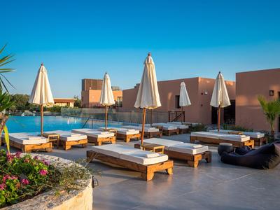 Area piscina dell'hotel con lettini e ombrelloni bianchi sotto un cielo limpido.