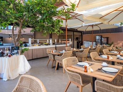 Restaurant en plein air avec tables en bois dressées, chaises et buffet sous de grands parasols.