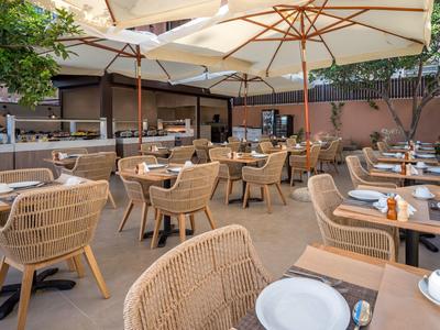 Große Terrasse mit vielen geflochtenen Stühlen, Holz-Tischen und weißen Sonnenschirmen.