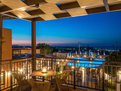 Balcone con area salotto, piscina illuminata e vista mare al tramonto.