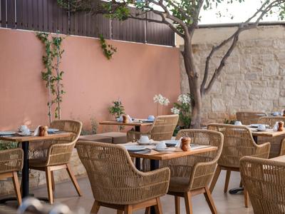 Accogliente terrazza con sedie di vimini e tavoli davanti a un muro rosa e recinzione di pietra.