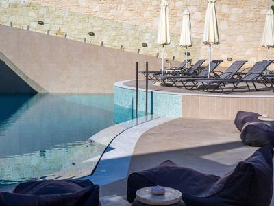 Piscina esterna moderna con lettini e ombrelloni davanti a un muro in pietra naturale.