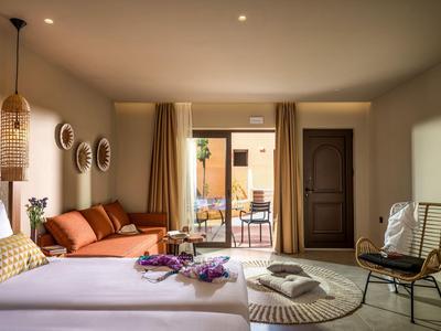 Bright hotel room with double bed, terrace access, sofa, and modern chair.