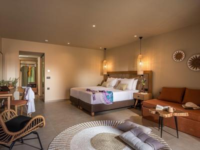 Modern hotel room with double bed, sofa, armchair, and cozy lighting.