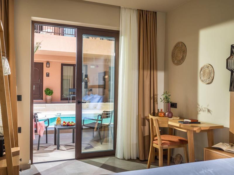 Helles Zimmer mit Holzmöbeln, Schreibtisch, Stuhl, Bett und Blick auf Terrasse mit Pool.