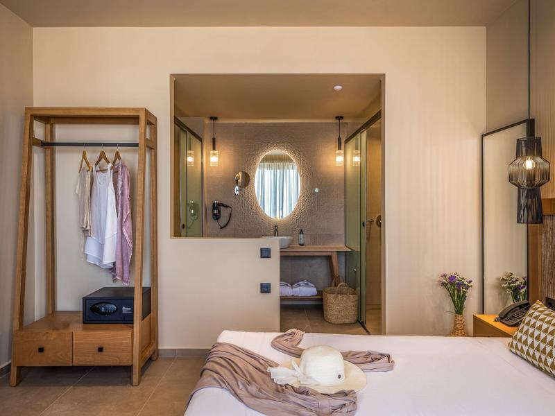 Modernes Schlafzimmer mit Holzmöbeln, Doppelbett, offenem Schrank und Blick ins Bad mit Spiegel.