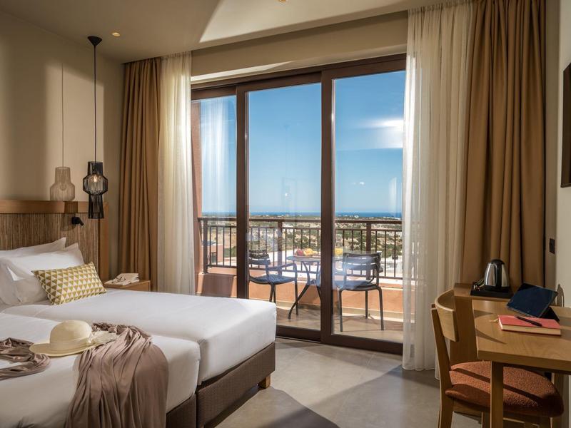 Modernes Hotelzimmer mit Doppelbett, Balkon, Holzmöbeln und Blick auf Stadt und Meer.