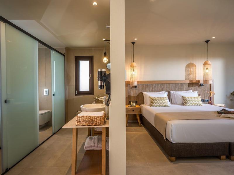 Modernes Hotelzimmer mit Doppelbett, elegantem Badezimmer mit Glaswand und warmem Licht.