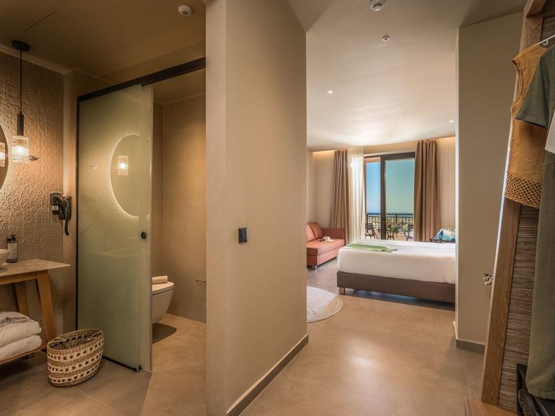 Moderner Hotelflur mit Bad links, Schrank rechts und Blick auf helles Schlafzimmer mit Meerblick.