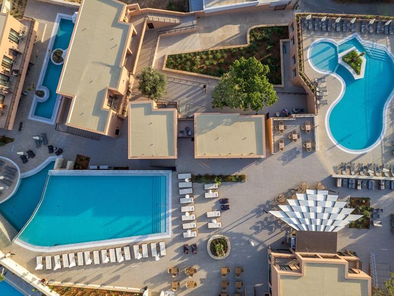Luftaufnahme eines Hotels mit zwei Schwimmbecken, Liegestühlen und begrünten Bereichen.