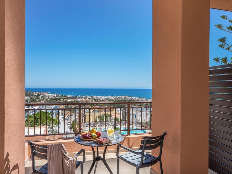 Balkon mit zwei Stühlen, kleinem Tisch, Obstschale und Meerblick unter blauem Himmel.