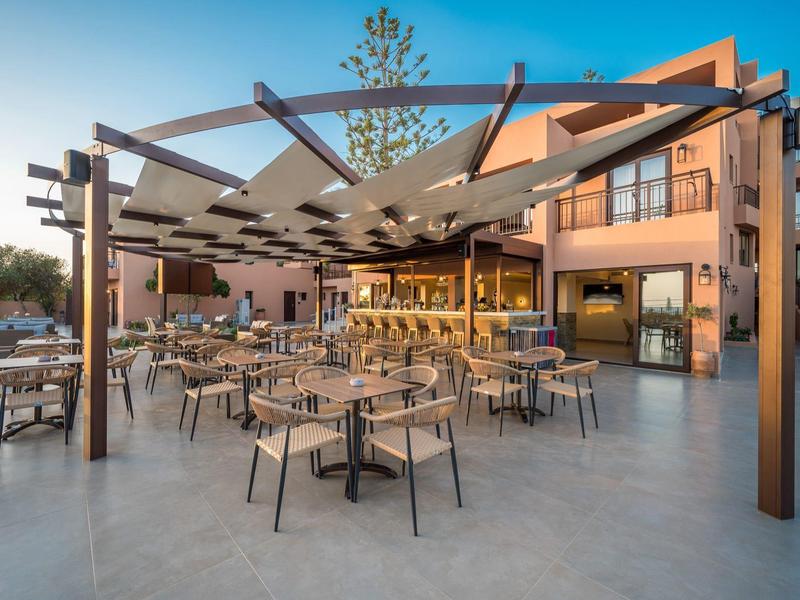 Moderner Außenbereich eines Cafés mit Stühlen, Tischen und Sonnenschutz, umgeben von Gebäuden.